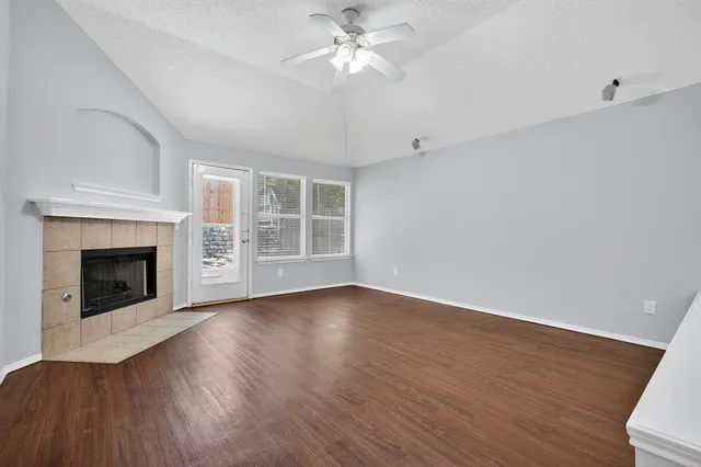 a view of an empty room with wooden floor fireplace and a window
