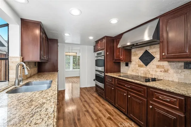 a kitchen with stainless steel appliances granite countertop wooden cabinets a sink dishwasher a stove and a refrigerator with wooden floor