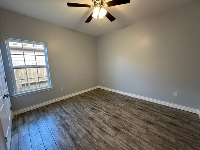 an empty room with wooden floor chandelier fan and windows