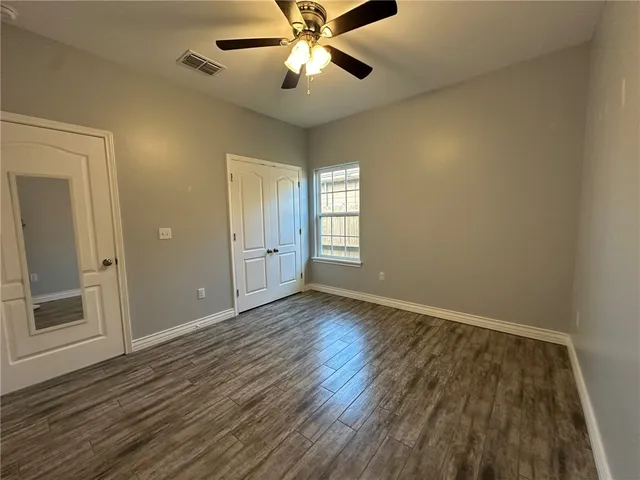 an empty room with wooden floor fan and windows