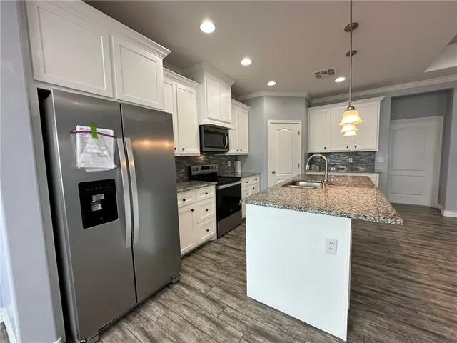 a kitchen with granite countertop a refrigerator a sink a stove and cabinets