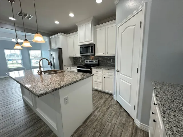 a kitchen with granite countertop a sink a counter top space stainless steel appliances and cabinets