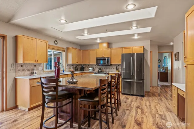 a kitchen with stainless steel appliances kitchen island granite countertop a refrigerator a stove a sink a dining table and chairs with wooden floor