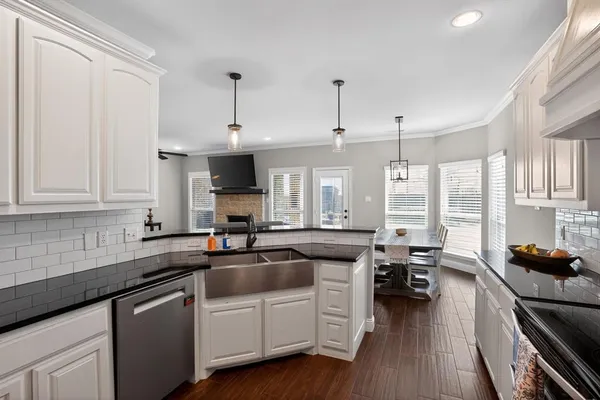 a kitchen with granite countertop a sink dishwasher stove and white cabinets with wooden floor