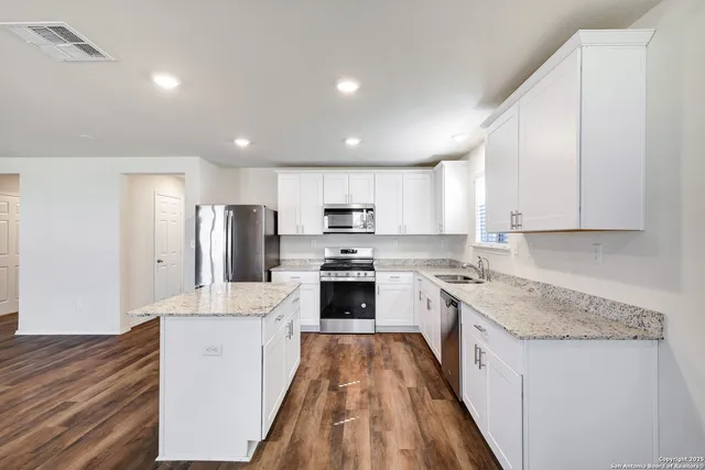 a large kitchen with stainless steel appliances granite countertop a stove a sink a refrigerator and white cabinets with wooden floor