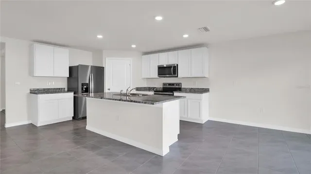 a kitchen with kitchen island a refrigerator a stove a sink a microwave and white cabinets