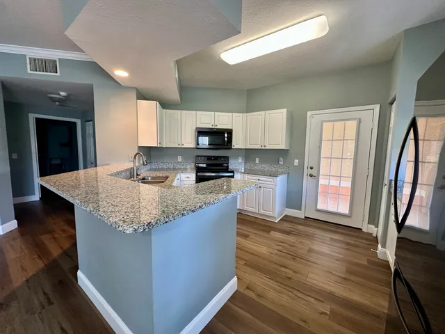 a kitchen with granite countertop a stove top oven a sink dishwasher and wooden cabinets with wooden floor