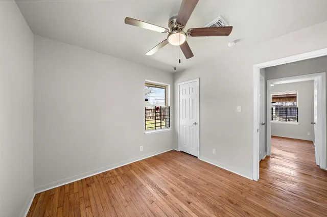 an empty room with wooden floor ceiling fan and windows