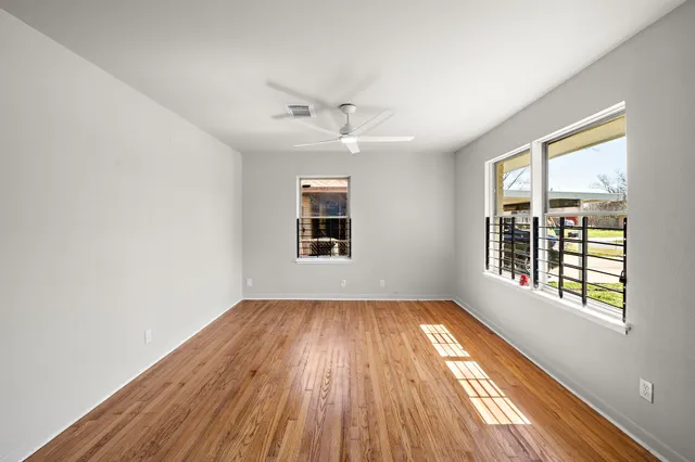 an empty room with wooden floor chandelier fan and windows