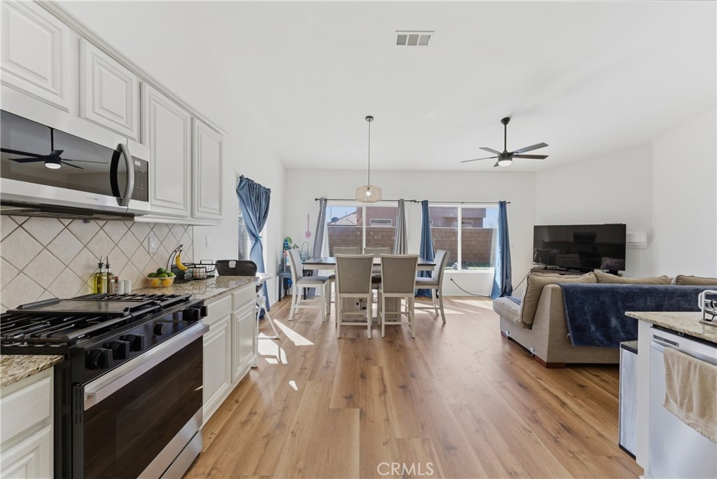 2036 East Jenner Street Lancaster, CA 93535 - Photo 14 of 50 a kitchen with stainless steel appliances a stove a sink a dining table and chairs with wooden floor