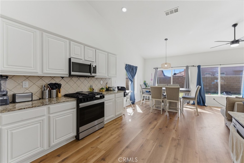 2036 East Jenner Street Lancaster, CA 93535 - Photo 15 of 50 a kitchen with stainless steel appliances granite countertop a stove top oven a sink dishwasher a dining table and chairs with wooden floor
