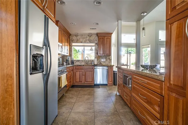 a kitchen with stainless steel appliances granite countertop a refrigerator a sink a stove and white cabinets with wooden floor