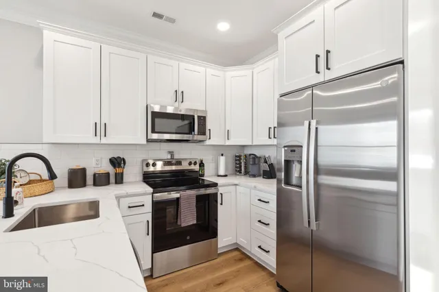 a kitchen with stainless steel appliances granite countertop a refrigerator a stove a sink and white cabinets