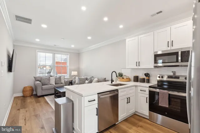 a view of kitchen with stainless steel appliances granite countertop a stove a sink a refrigerator and white cabinets with wooden floor