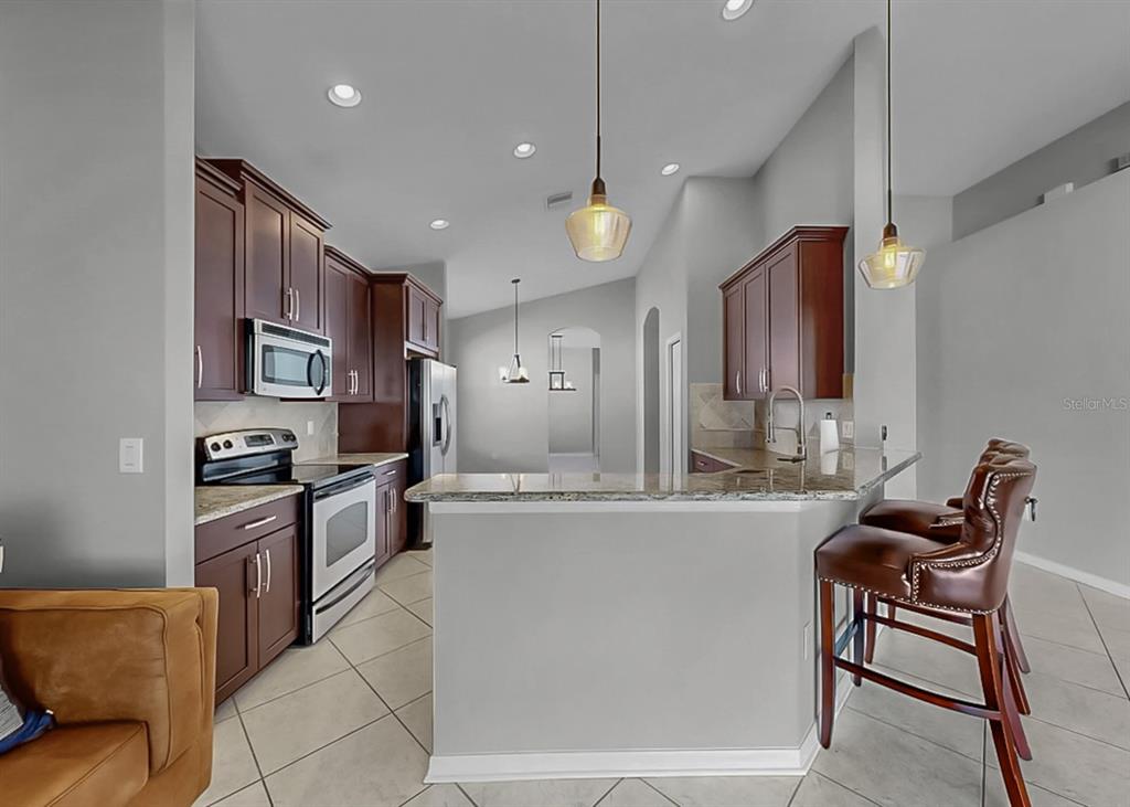 7109 Spindle Tree Lane Riverview, FL 33578 - Photo 29 of 42 a large kitchen with stainless steel appliances kitchen island granite countertop a refrigerator a stove a sink a dining table and chairs with wooden floor