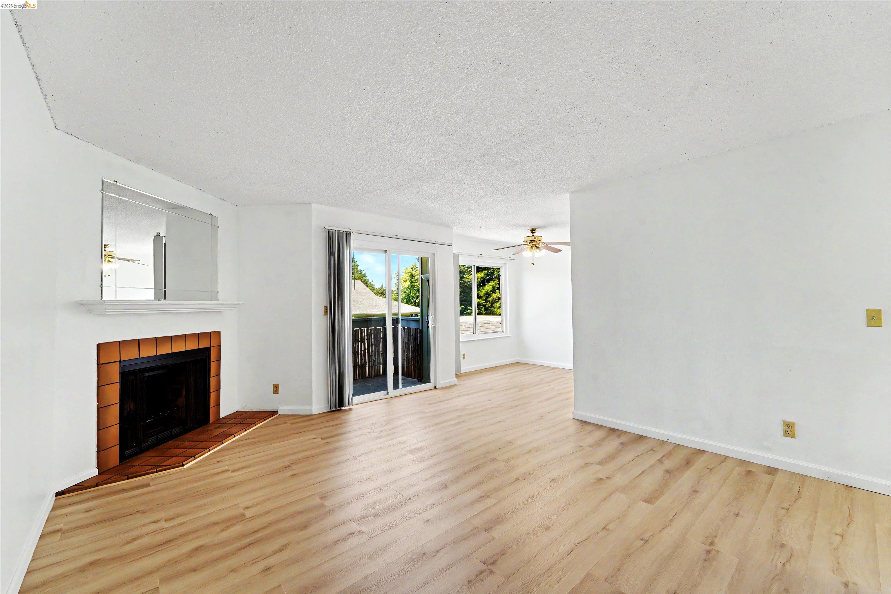 4186 San Pablo Dam Road, Unit A El Sobrante, CA 94803 - Photo 9 of 34 Spacious room featuring wood-finish flooring, a fireplace with a tile surround and hearth, white walls, and a sliding glass door to an exterior balcony