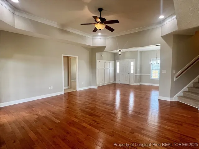 a view of an empty room with wooden floor and a ceiling fan
