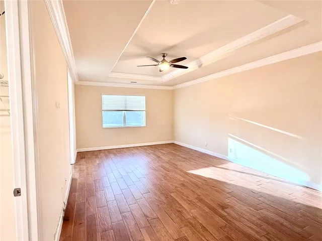 an empty room with wooden floor chandelier fan and windows