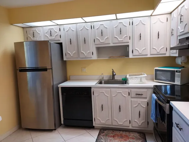 a kitchen with stainless steel appliances granite countertop a refrigerator a stove a sink and white cabinets with wooden floors