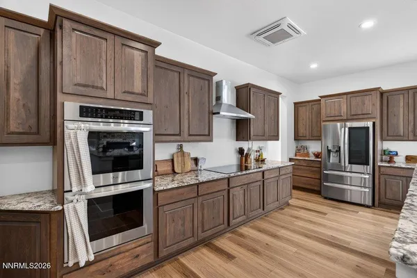 a kitchen with stainless steel appliances kitchen island granite countertop a stove top oven a sink dishwasher and a refrigerator with wooden cabinets