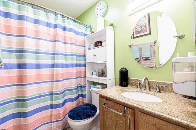a bathroom with a granite countertop sink a toilet a mirror and shower curtain