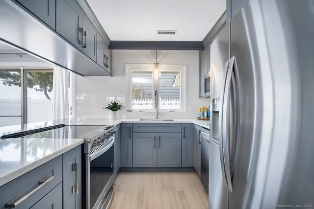 a kitchen with stainless steel appliances granite countertop a refrigerator a sink dishwasher a stove and white countertops with wooden floor