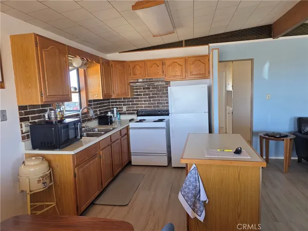 a kitchen with stainless steel appliances granite countertop a refrigerator a sink dishwasher a stove and white countertops with wooden floor