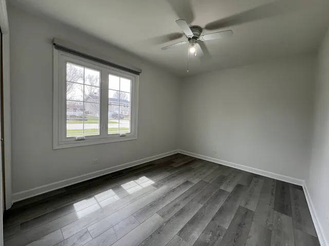 an empty room with wooden floor fan and windows