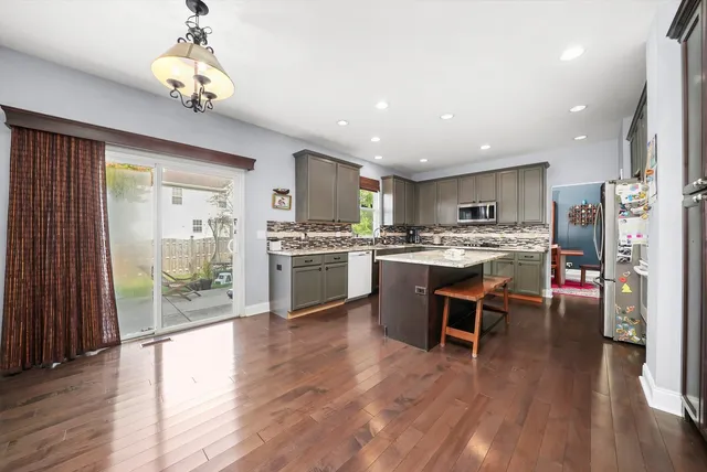 a open kitchen with stainless steel appliances granite countertop a stove top oven a refrigerator a dining table and chairs with wooden floor