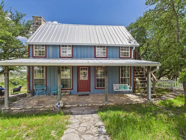 a view of a white house with a yard potted plants and large tree