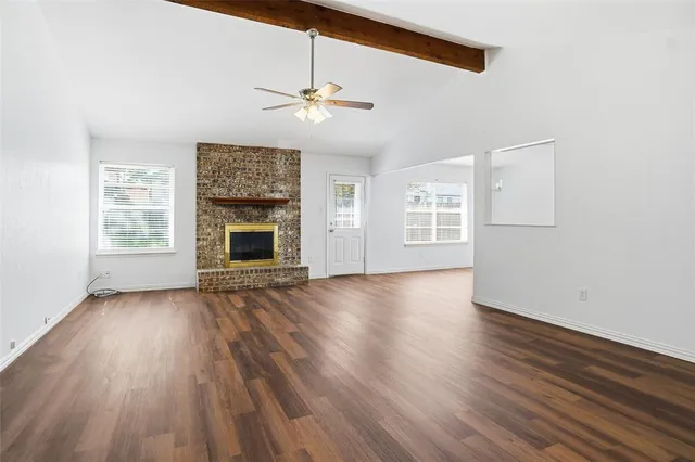 an empty room with wooden floor fireplace and windows