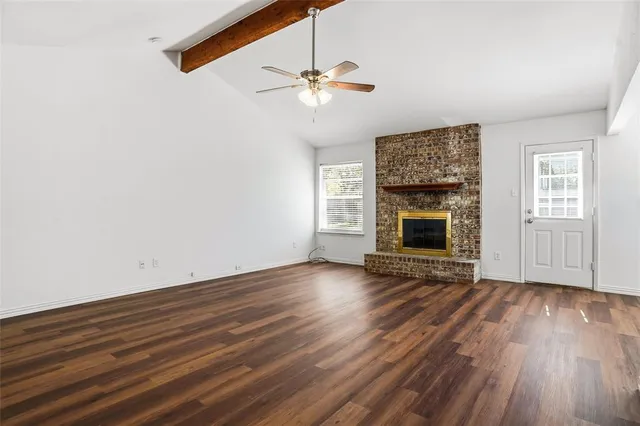 an empty room with wooden floor fireplace and windows