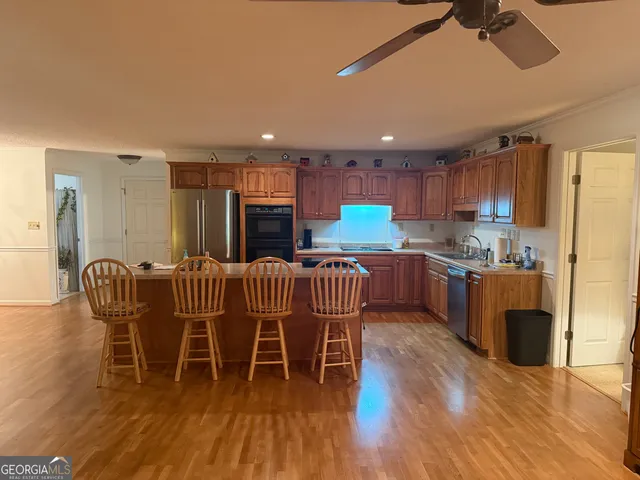 a open kitchen with stainless steel appliances granite countertop a refrigerator a stove a sink dishwasher and a dining table with wooden floor