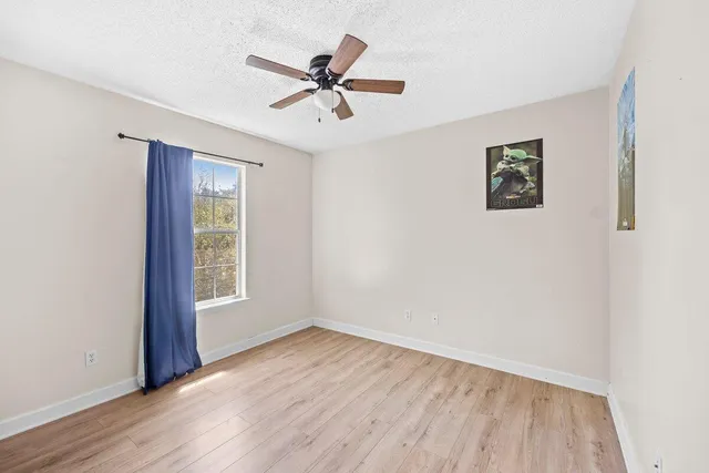an empty room with wooden floor fan and windows