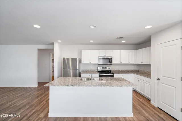 a kitchen with kitchen island granite countertop a stove top oven a sink and white cabinets