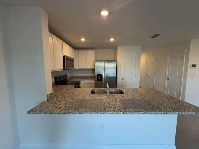 a large kitchen with granite countertop a sink a counter top space and stainless steel appliances