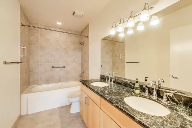a bathroom with a granite countertop tub sink double vanity and mirror