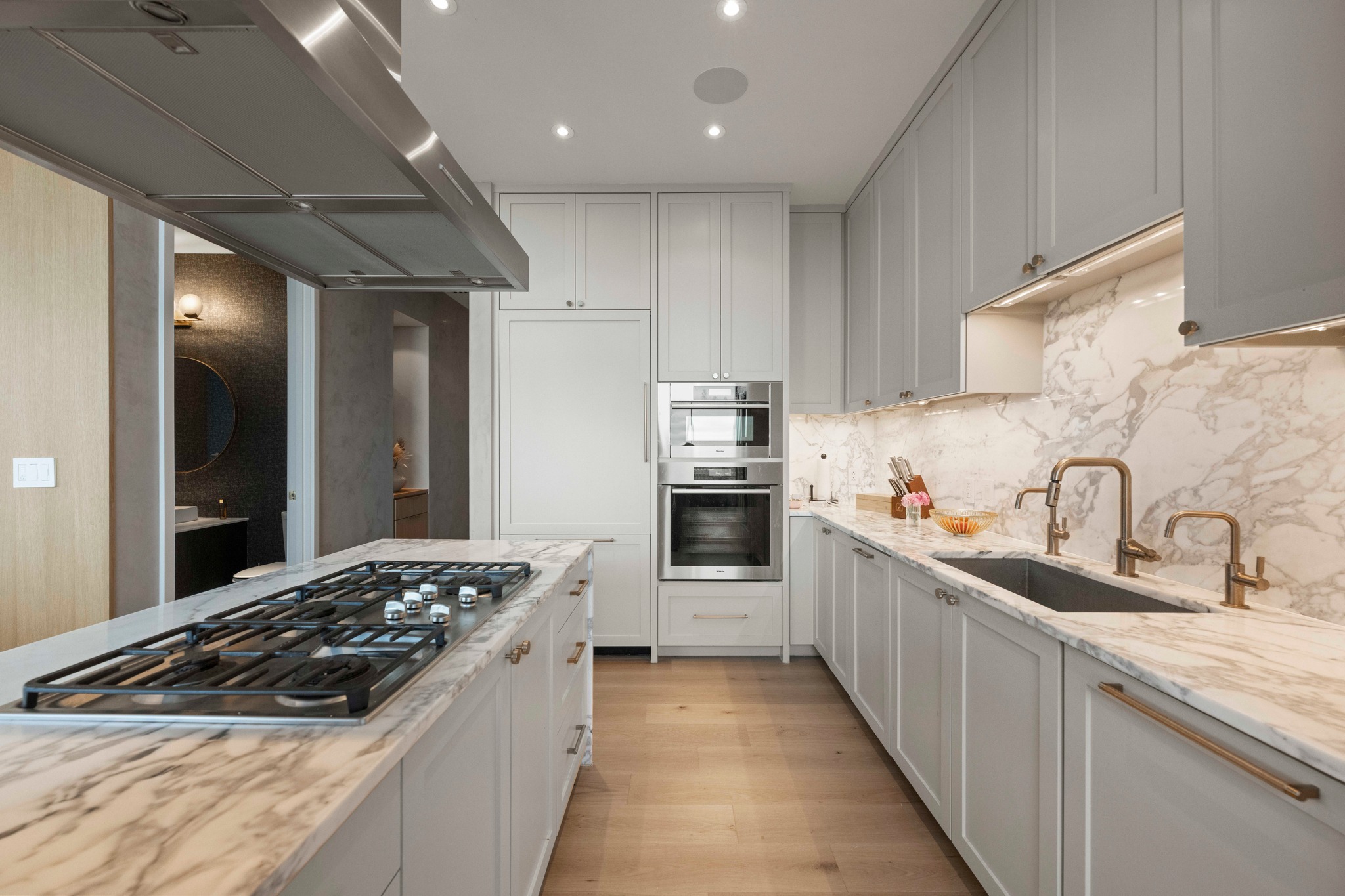 210 Lavaca Street, Unit 2706 Austin, TX 78701 - Photo 25 of 32 Gourmet kitchen featuring a substantial island with a built-in gas range, white shaker cabinetry, integrated stainless steel appliances, marble countertops and backsplash, and light wood-finish flooring