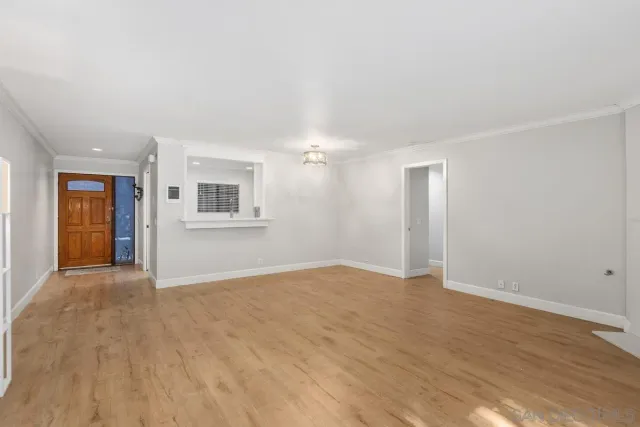 a view of an empty room with wooden floor and kitchen space