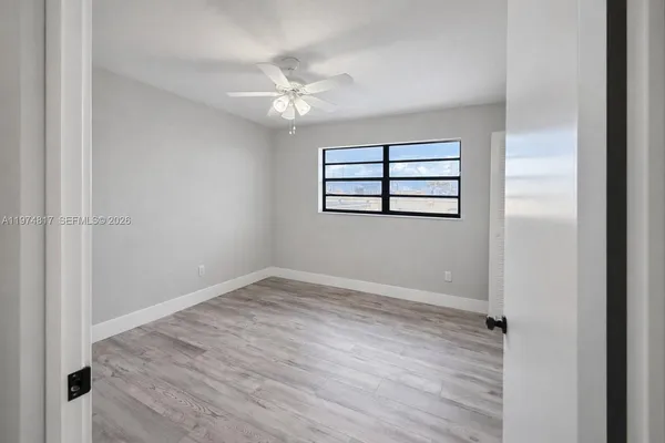an empty room with wooden floor chandelier fan and windows