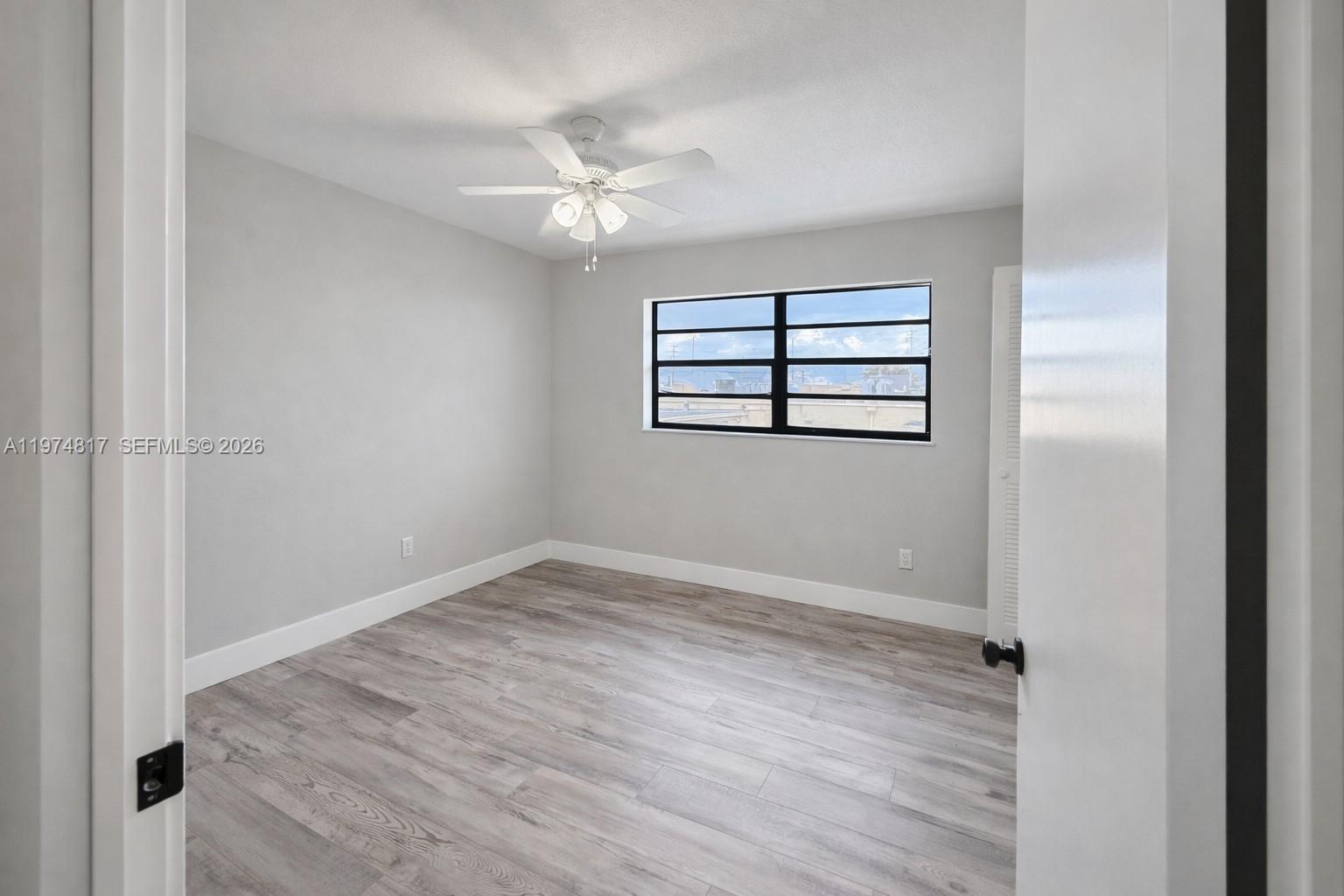 5935 West 16th Lane Hialeah, FL 33012 - Photo 8 of 15 an empty room with wooden floor chandelier fan and windows