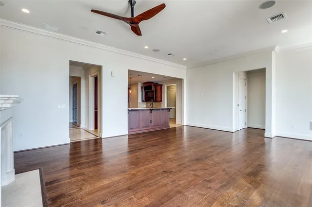 a view of an empty room with wooden floor and a ceiling fan