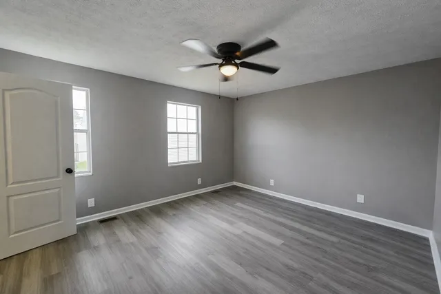 an empty room with wooden floor a ceiling fan and windows