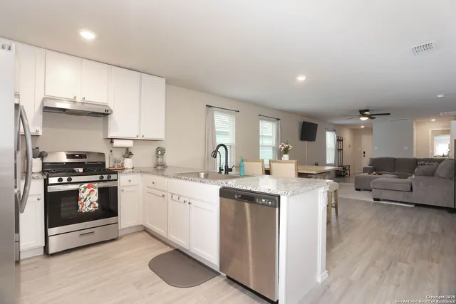 a kitchen with stainless steel appliances granite countertop a stove top oven a sink dishwasher and white cabinets with wooden floor