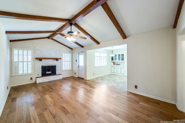 a view of an empty room with wooden floor fireplace and a window
