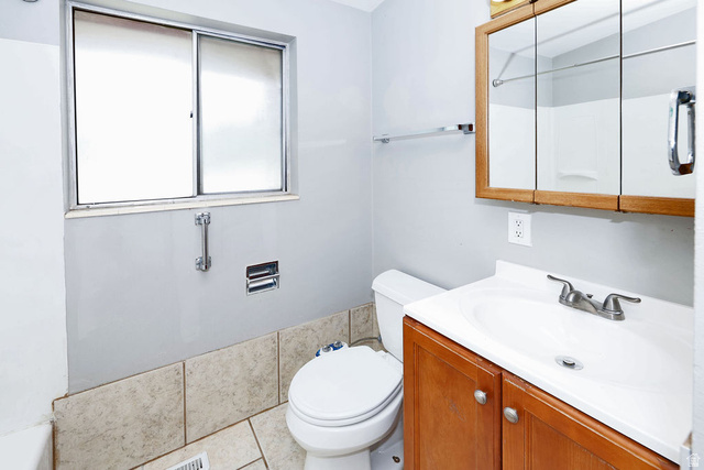 1272 Cook Street Ogden, UT 84404 - Photo 15 of 46 Bathroom featuring a sliding window, a wood-finish vanity with an integrated sink, a mirrored medicine cabinet, and tiled wainscoting