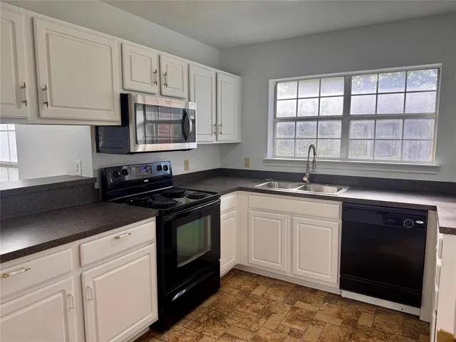a white kitchen with granite countertop a stove a sink and a microwave
