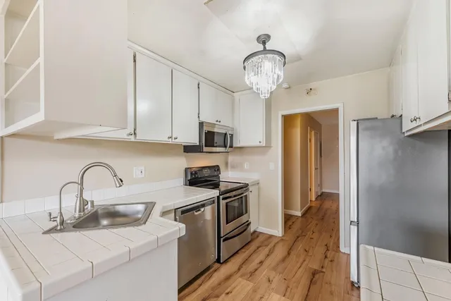 a kitchen with stainless steel appliances granite countertop a sink a stove a refrigerator cabinets and a dining table with wooden floor