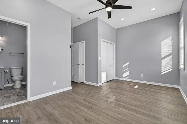 a view of an empty room with wooden floor and a ceiling fan