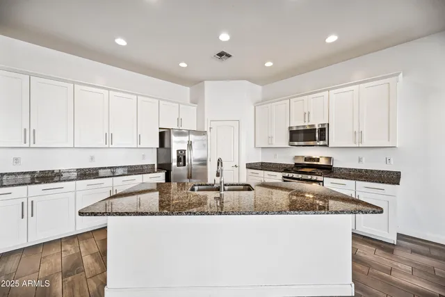 a kitchen with stainless steel appliances granite countertop a stove a sink a refrigerator a microwave and white cabinets